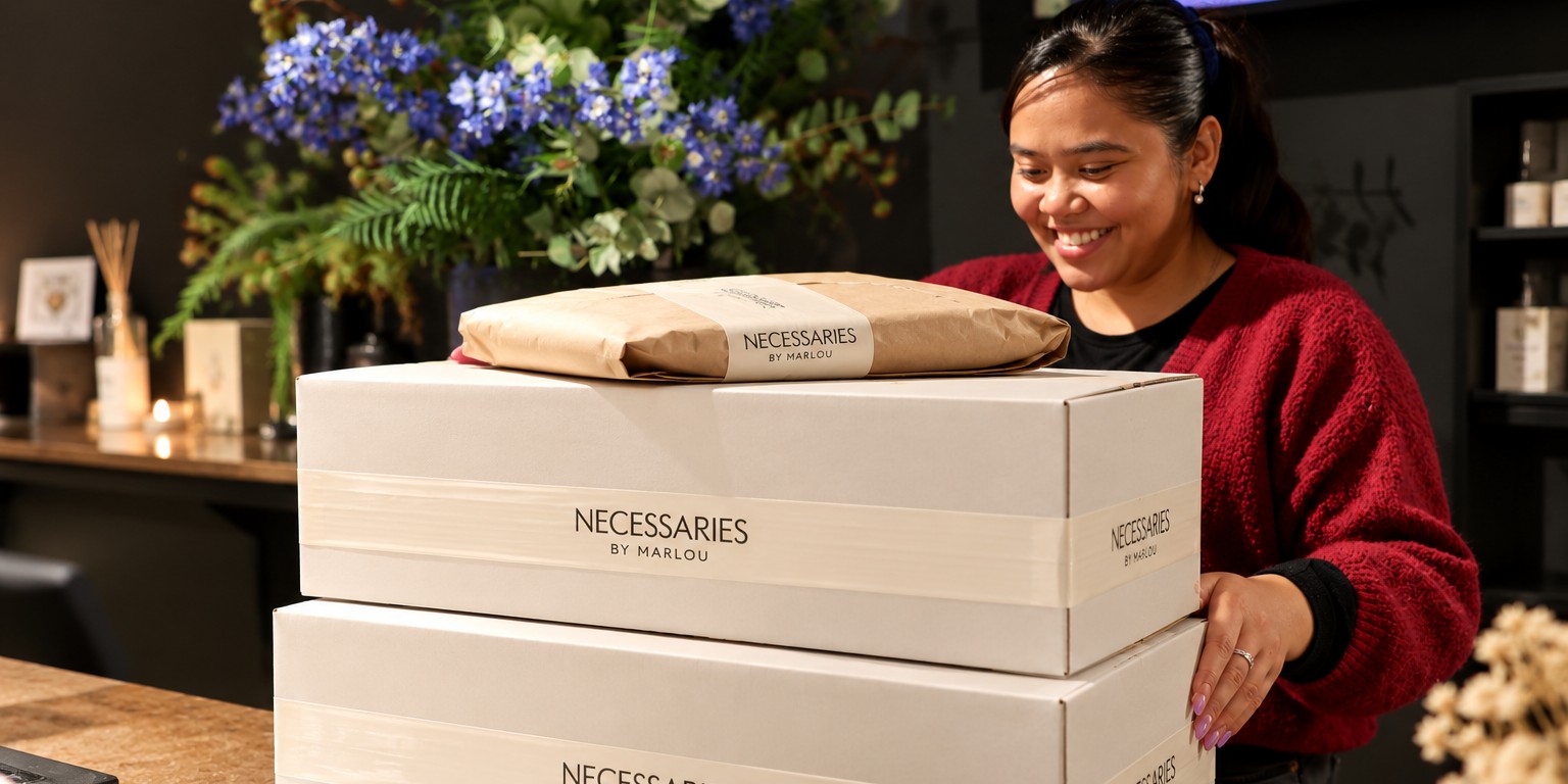 Medewerkster van Necessaries by Marlou maakt webshopbestellingen klaar voor verzending in de winkel in Deventer, met zorgvuldig verpakte pakketten voorzien van de eigen verpakkingstape.
